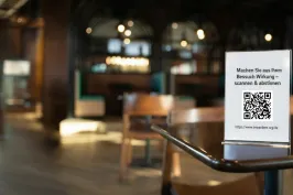 Tischaufsteller mit QR-Code, der Gäste einlädt, zu scannen und abzustimmen, um lokale Projekte zu unterstützen.