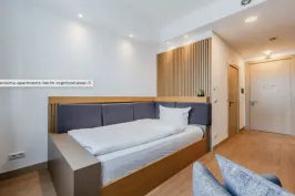 Modernes, helles Hotelzimmer mit Einzelbett, Holzboden und minimalistischer Einrichtung.