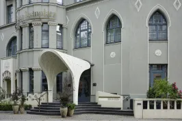 Gebäude mit rundem Vordach, großen Fenstern und Blumenkübeln am Eingang.