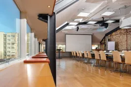 Heller Konferenzraum mit langen Tischen, Holzstühlen und großer Fensterfront