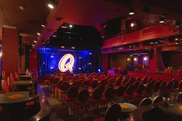 Roter Theatersaal mit runden Tischen, Bühne und beleuchtetem Q im Hintergrund