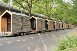 Reihe moderner Tiny Houses auf Anhängern unter Bäumen an einer Straße.
