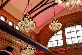 Mehrere Kronleuchter hängen an einer Backstein-Decke mit großen Fenstern und pinkem Licht.