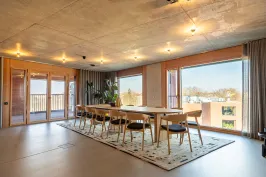 Moderner Konferenzraum mit langem Holztisch, Stühlen und großen Fenstern mit Ausblick.