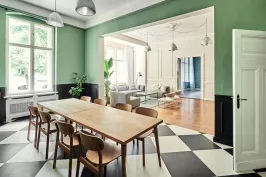 Großer heller Raum mit langem Holztisch, Stühlen und Schachbrettboden, angrenzendes Wohnzimmer.