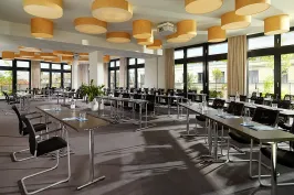 Heller Konferenzraum mit vielen Tischen, Stühlen und großen Fenstern