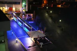 Beleuchtete Terrasse mit Sonnenschirmen und blau-violettem Licht bei Nacht