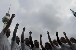 Gruppe von Menschen zeigt nach oben, Fernsehturm im Hintergrund, bewölkter Himmel.