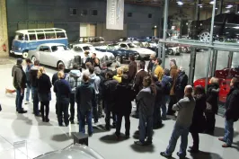 Gruppe Menschen in einer Oldtimerausstellung, umgeben von klassischen Autos.