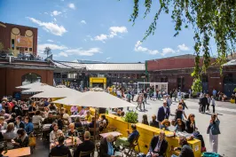 Menschen genießen sonniges Wetter unter Sonnenschirmen auf einem belebten Platz