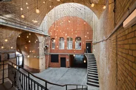 Großer Backsteinraum mit Gewölbedecke, Hängelampen und breiter Treppe.