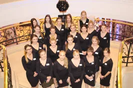 Gruppe junger Frauen in schwarzen Kleidern auf einer Treppe, alle schauen in die Kamera.