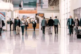 Menschen gehen durch eine helle, moderne Halle mit Glasfronten und glänzendem Boden.