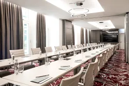 Konferenzraum mit langen Tischen, weißen Stühlen und moderner Beleuchtung