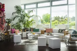 Helles Wohnzimmer mit modernen weißen Möbeln, Pflanzen und großen Fenstern.