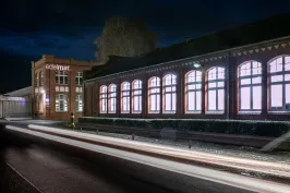 Beleuchtetes Backsteingebäude bei Nacht mit Lichtspuren auf der Straße.