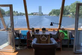 Steuerstand eines Bootes mit Ausblick auf einen Fluss und einen fernen Turm bei Sonnenschein.
