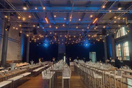 Festlich gedeckter Saal mit langen Tischen, dekoriert mit Lichterketten.