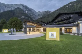 Modernes Gebäude mit Kunstinstallationen im beleuchteten Außenbereich und Bergen im Hintergrund.