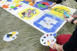 Mehrere Personen bemalen gemeinsam ein großes Puzzle-Bild mit bunten Farben.