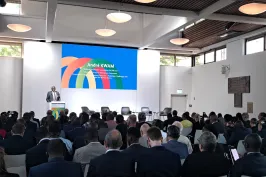 Mann spricht bei Konferenz vor großem Publikum, bunte Präsentation im Hintergrund.