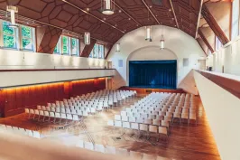 Festsaal Blick von der Empore in den Saal mit Reihenbestuhlung und Bühne mit blauem Vorhang