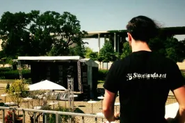 Mann mit schwarzem T-Shirt blickt auf eine leere Open-Air-Bühne im Park.