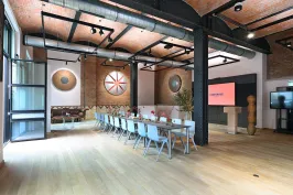 Moderner Konferenzraum mit langem Tisch, Stühlen und Präsentationsbildschirm.