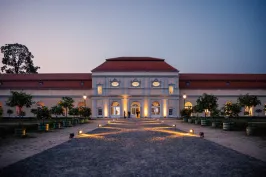 Beleuchtetes barockes Gebäude mit rotem Dach und symmetrischem Vorplatz bei Dämmerung.