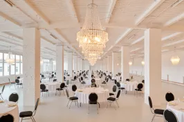 Großer, heller Festsaal mit runden Tischen, schwarzen Stühlen und Kronleuchtern.