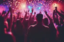 Menschenmenge feiert bei Konzert, bunte Lichter und Konfetti in der Luft.