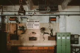 Werkloft Alte Werkstatt mit grünen Spinden, Holztisch und Wanddeko unter industrieller Decke.