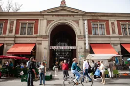 Menschen vor einem historischen Markthallengebäude mit roten Markisen und Ständen.