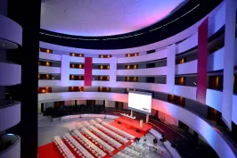 Modernes Konferenzzentrum mit runden Balkonen, roten Teppichen und beleuchteter Bühne.