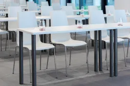 Helle Seminarraumreihe mit weißen Stühlen und Tischen, Wassergläser bereitgestellt.