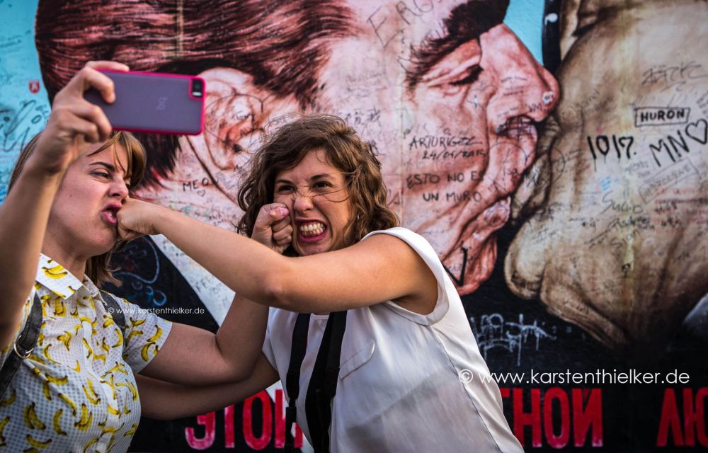 Zwei Mädchen machen Selfies vor der Berliner Mauer