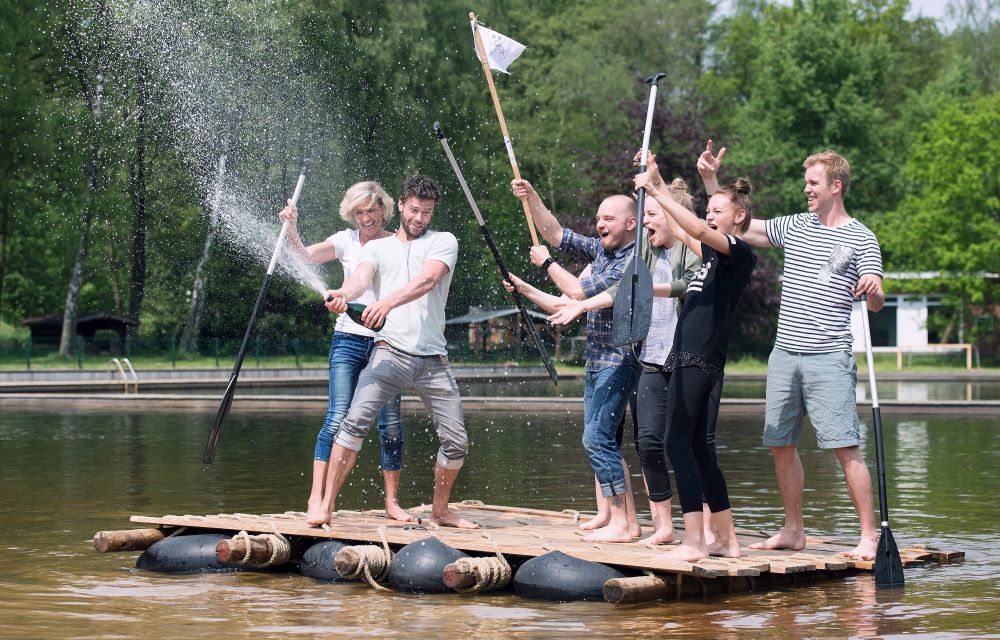 Eine Gruppe von Menschen steht auf einem selbstgebauten Floss und spritz mit Champagner