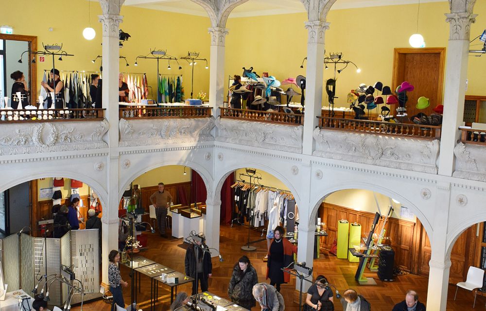 People and exhibition tables at an exhibition in the hall of Villa Elisabeth
