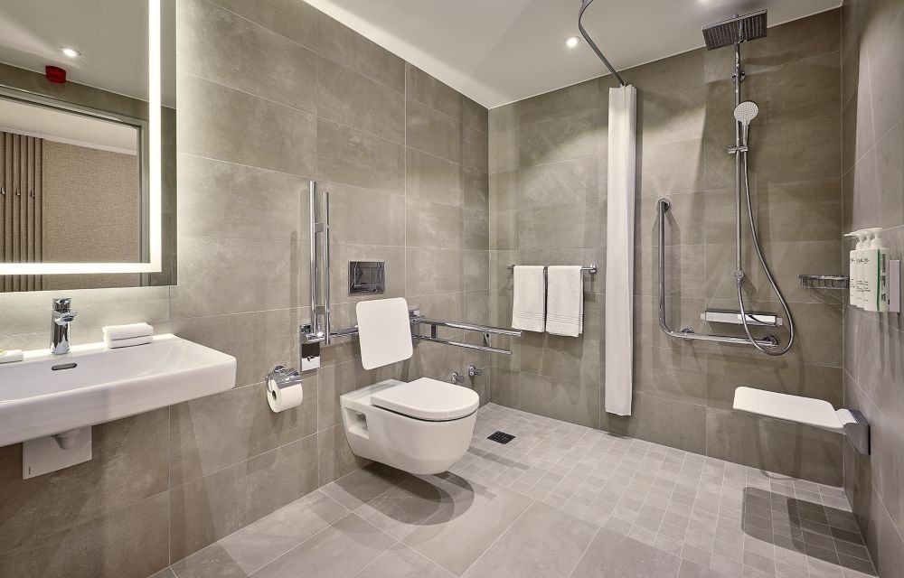 Badezimmer mit abgesenktem Waschbecken, ebenerdigen Dusche, und Toilette mit Haltegriffen