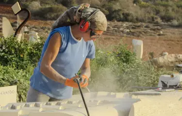 Steinbildhauer mit Schutzbrille und Bohrmaschine bei der Arbeit.