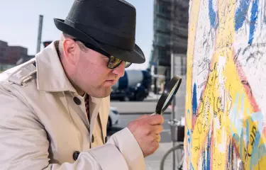 Meeting Guide Berlin Team spirit inspector with magnifying glass examines section of wall
