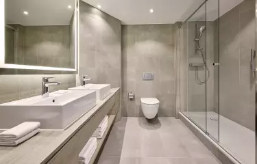 Badezimmer mit Dusche, Toilette, zwei Waschbecken und einem großen Spiegel