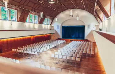 Festsaal Blick von der Empore in den Saal mit Reihenbestuhlung und Bühne mit blauem Vorhang