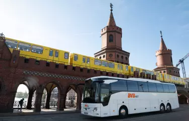 Ein BVB.net Reisebusse fährt auf der Straße in Berlin, in Hintergrund eine U-Bahn.