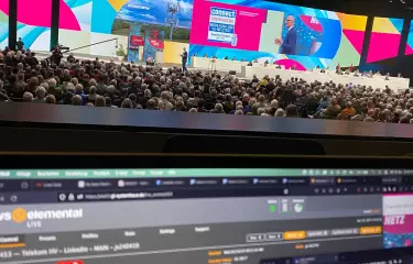Ein großes Publikum verfolgt die Hauptversammlung der Deutschen Telekom. Im Vordergrund ist ein Bildschirm zu sehen, der den Cloud-Encoder und den LinkedIn-Stream für die Veranstaltung überwacht.