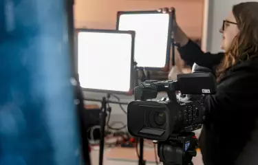 Eine Person stellt eine Beleuchtung neben einer Kamera auf.