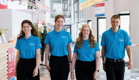 Vier lächelnde Personen, die auf die Kamera zulaufen kommen und blaue T-Shirts mit der Aufschrift "Tremfya" tragen.