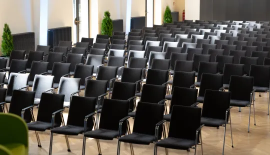 Reihen leerer schwarzer Stühle in einem hellen Konferenzraum