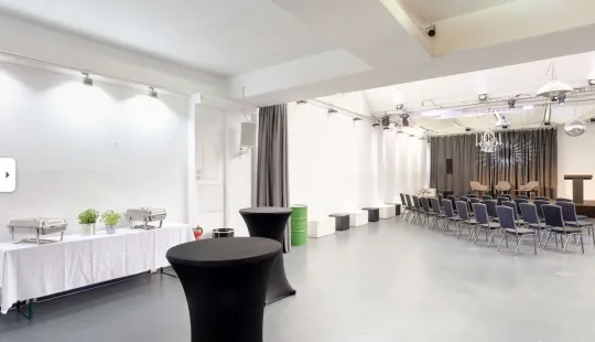 Moderner, heller Veranstaltungsraum mit Stehtischen, Catering mit Dekoration und Stuhlreihen