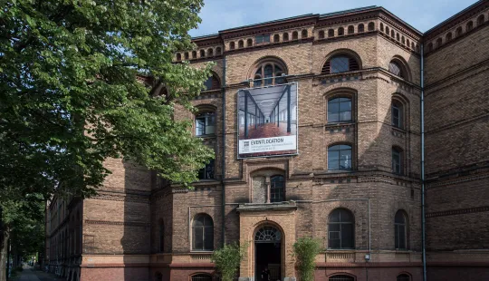 Backsteingebäude mit großem Banner am Eingang und zwei Pflanzen davor
